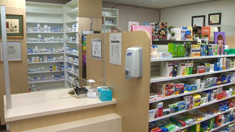 A pharmacy desk with pill bottles behind it stands beside a shelf with medication.